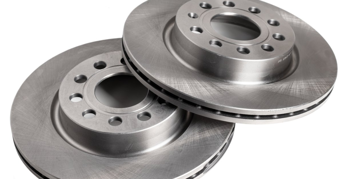 Two silver ventilated brake rotors are lying on their sides on a white surface and overlapping each other.