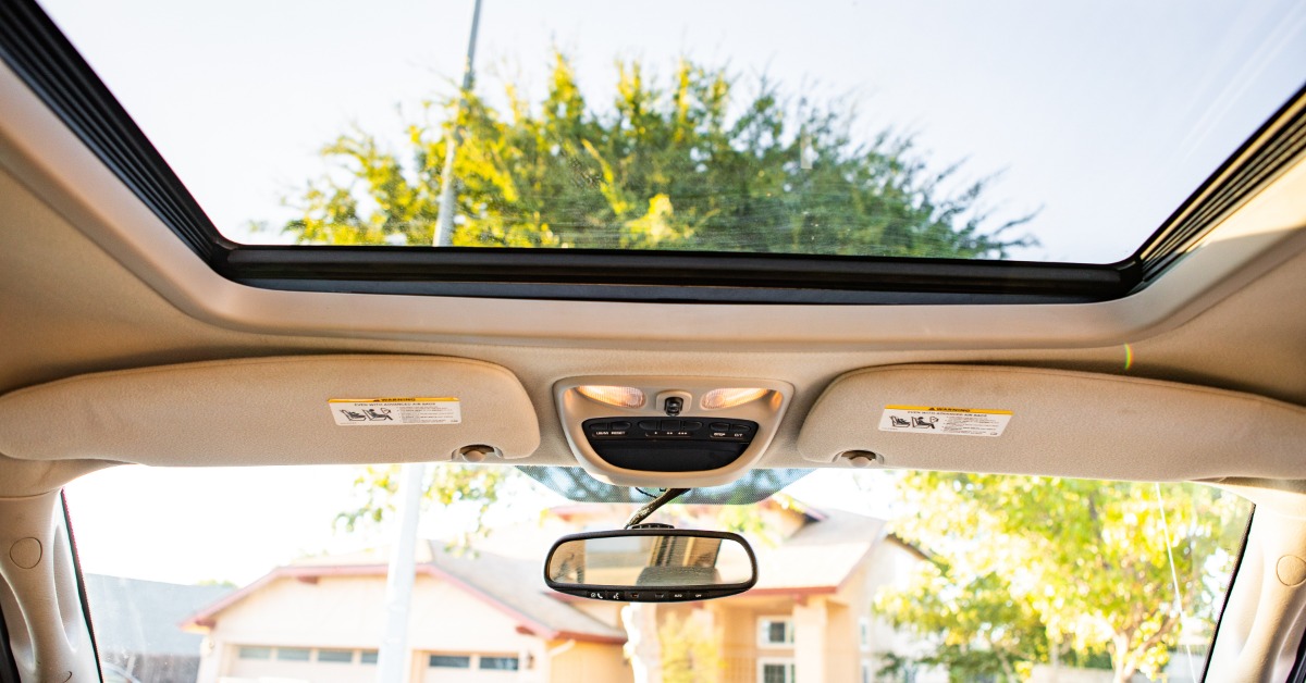 A beige pickup truck interior with a large glass sunroof, overhead controls, and a rearview mirror facing houses.