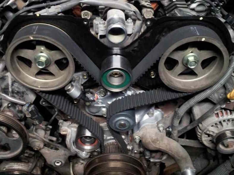A smaller, thinner timing belt is in place under the hood of a car. The belt is black and the other components are silver.