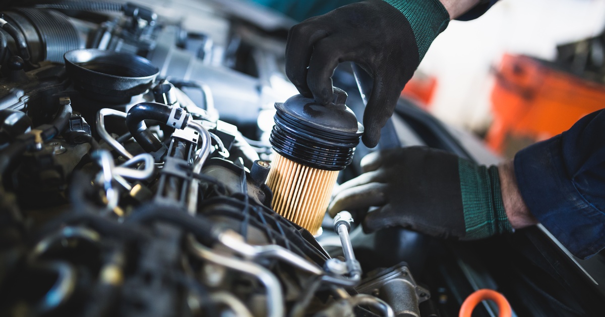 At close range, a person wearing black gloves places a clean oil and fuel filter into the engine of a vehicle.