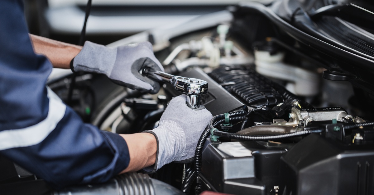A mechanic wearing a blue shirt and gray gloves uses a torque wrench to tighten a component on the engine of a car.