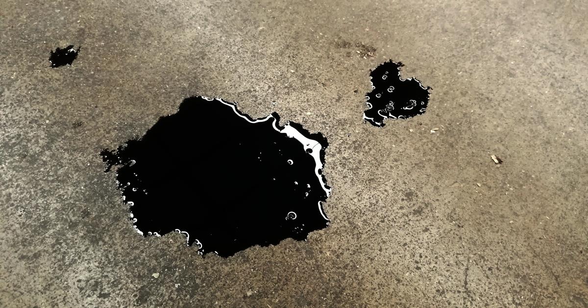 A close-up of some black oil splotches on concrete. There is one big spot and two smaller spots.
