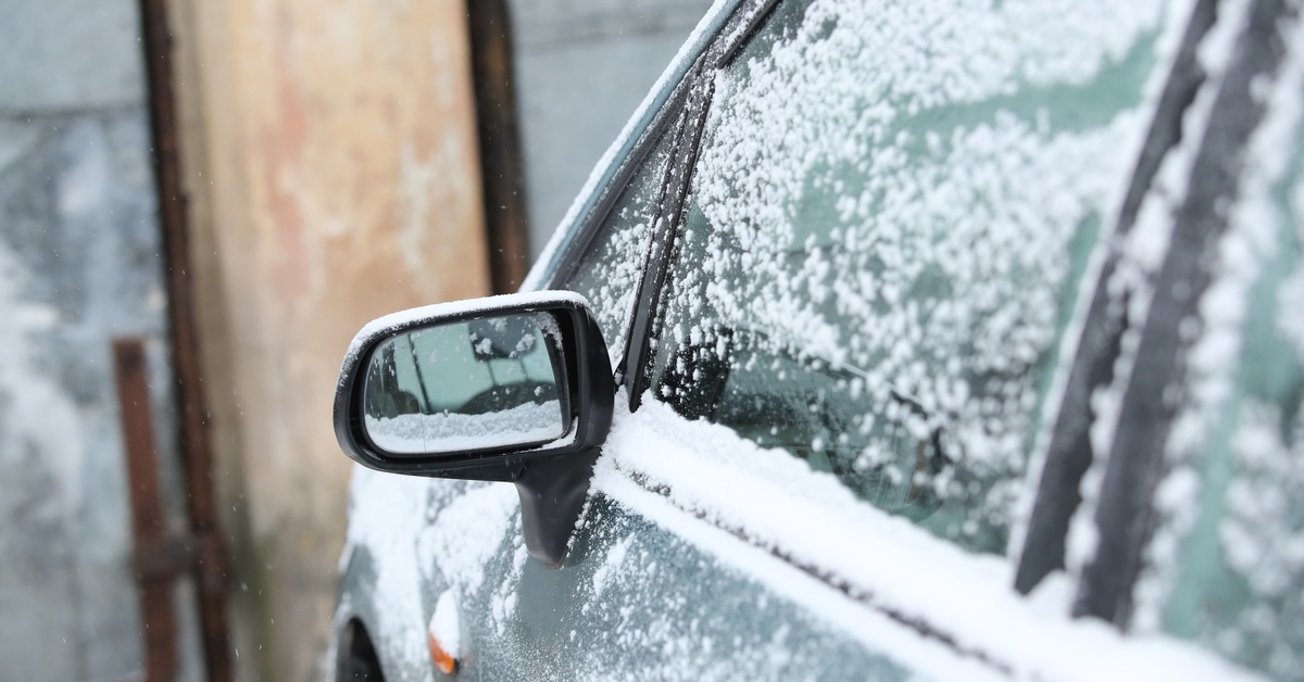 A vehicle parked outside. The driver's side window and the side view mirror have speckles of snow on the surface.