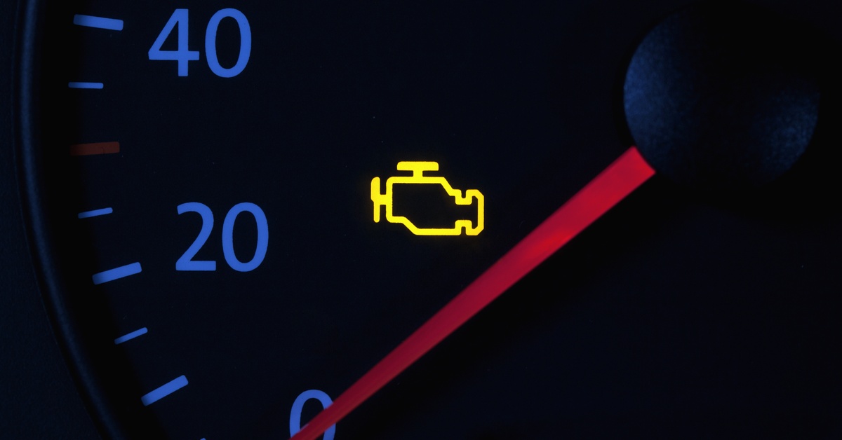 A close-up of a vehicle speedometer with an illuminated check engine light. The needle is pointed toward 0.