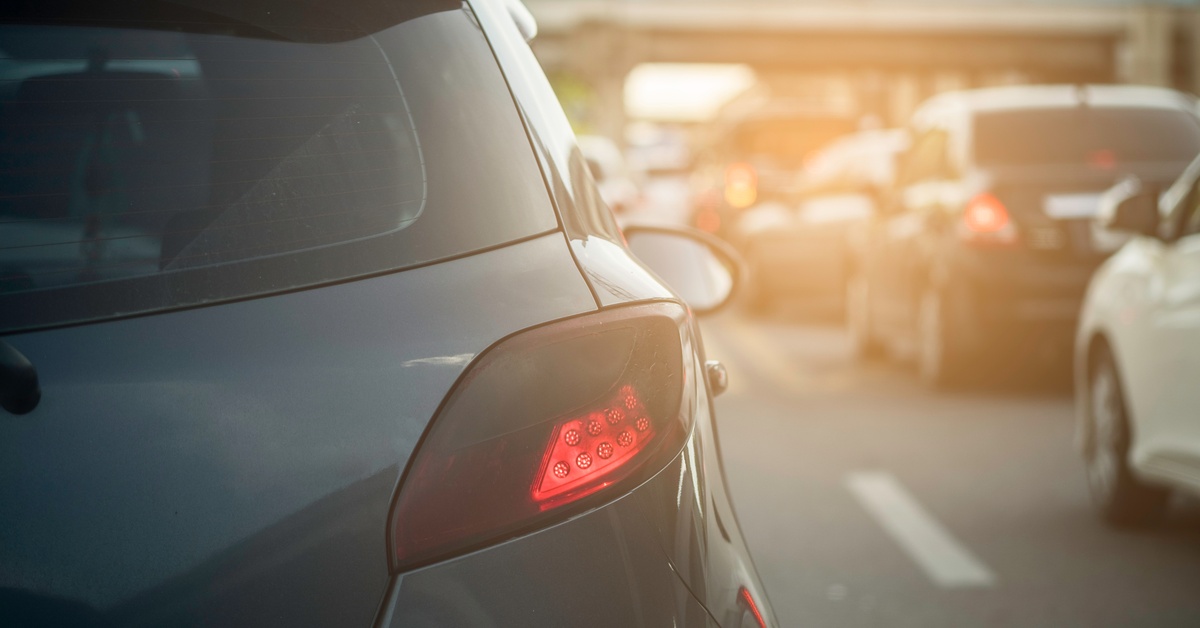 A black car parked in the middle of an urban street, approaching an overpass. There is heavy traffic on the road.