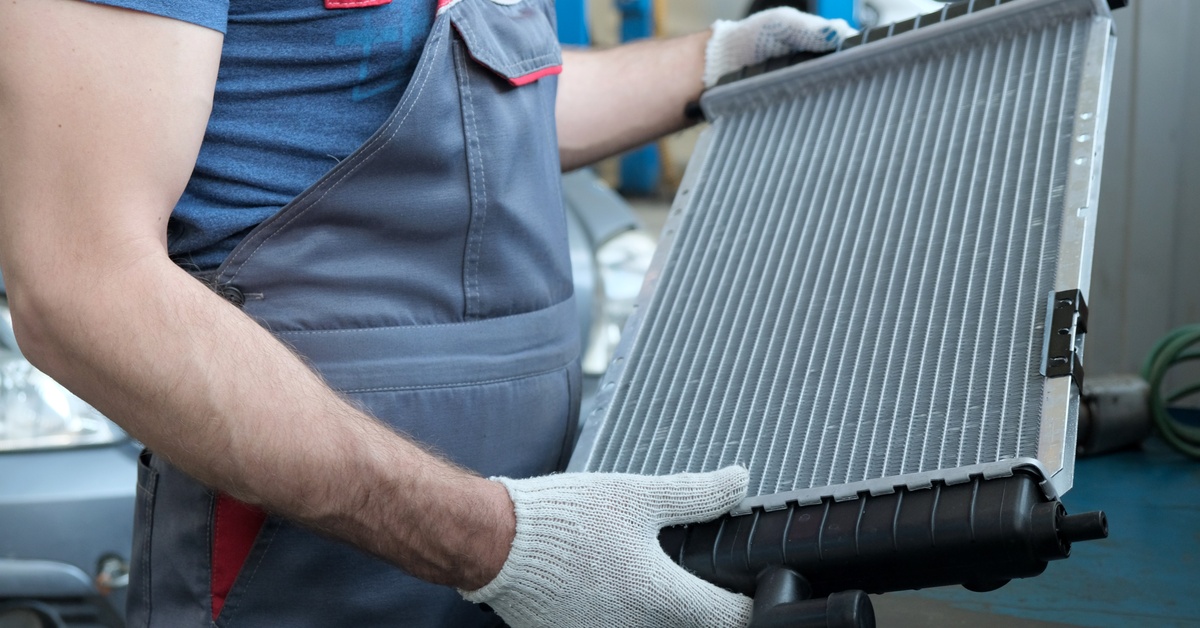 How To Tell if Denso Toyota Parts Are Authentic In a workshop, a mechanic wearing an apron and a pair of white gloves holds and examines a new radiator.