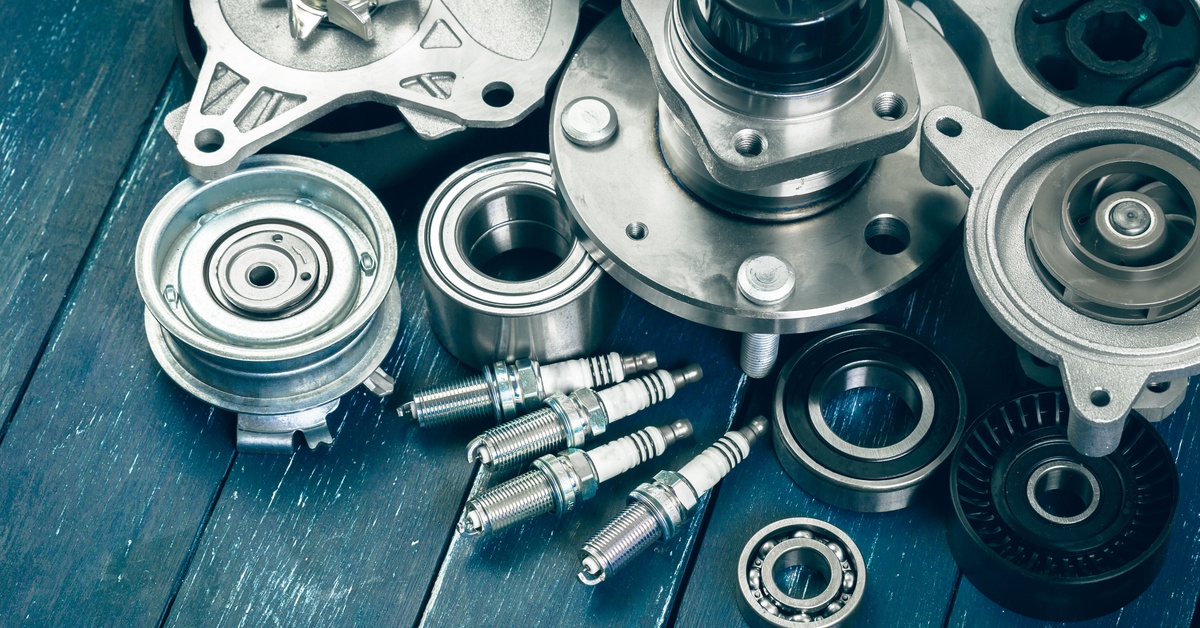 An array of silver car parts, including spark plugs and wheel bearings, is sitting on a surface made of wooden planks.