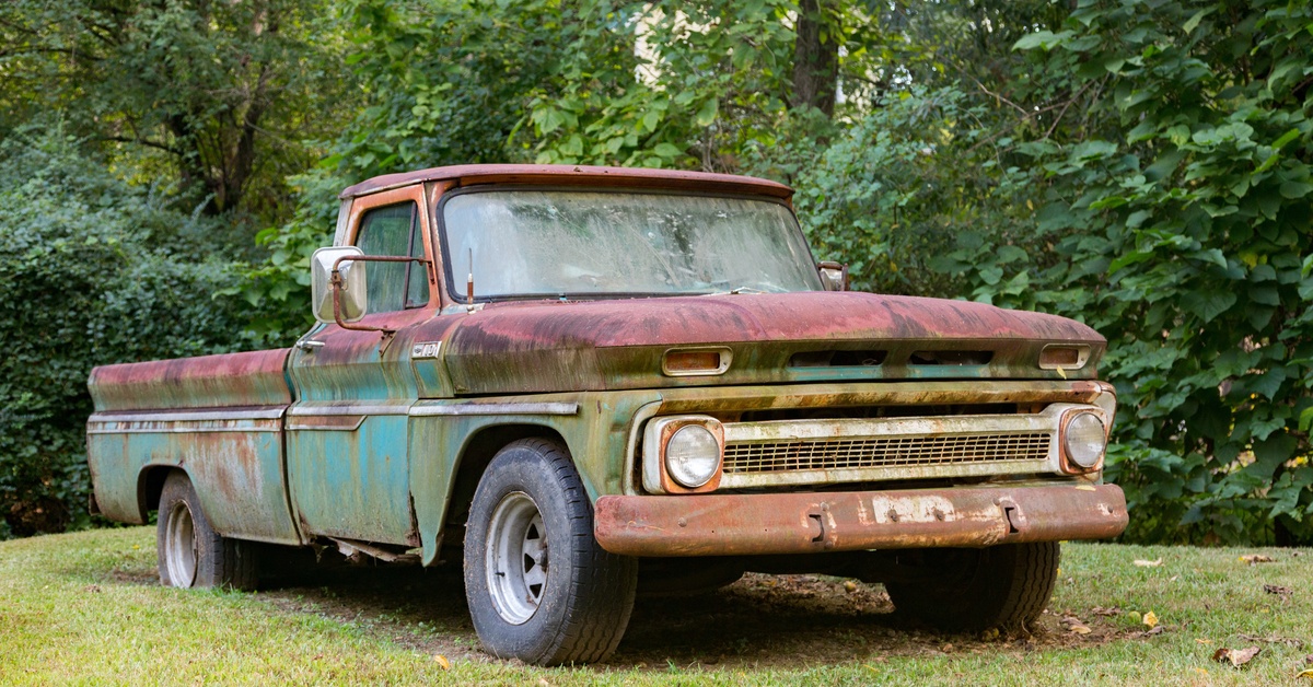 Sourcing Rare Toyota Pickup Body Panels for Restoration A vintage truck is parked in front of trees. The vehicle is blue and red with rust spots on the side panels and hood.