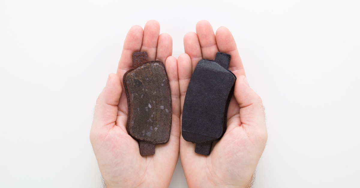 Two hands are cupping two brake pads side by side. One brake pad is rusted and dented, the other is dark and smooth.