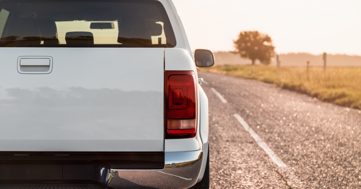 The backside of a white truck driving down an asphalt road. A field with a fence is in the background. The backside of a white truck driving down an asphalt road. A field with a fence is in the background.