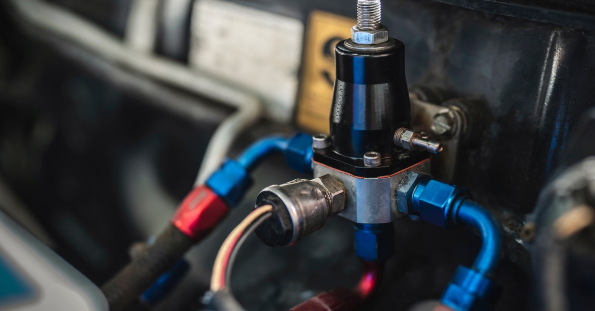 A close-up of a fuel regulator installed in the engine of a car. Blue connectors extend from the regulator.