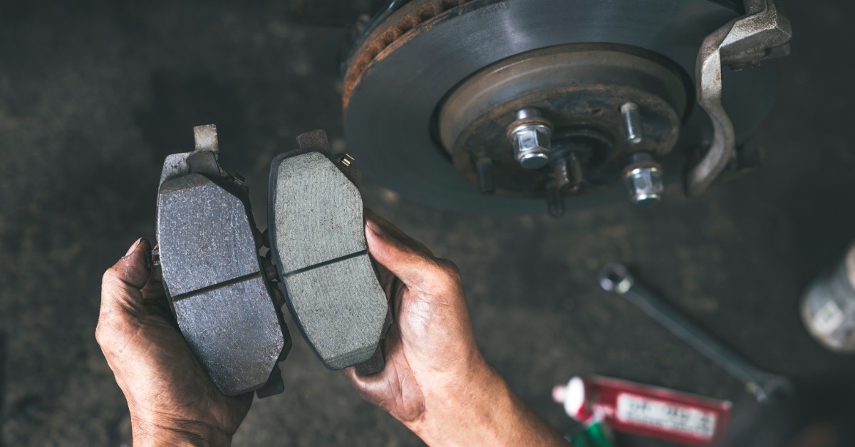 An overhead view of a person holding new and worn brake pads side by side, showing different thicknesses.