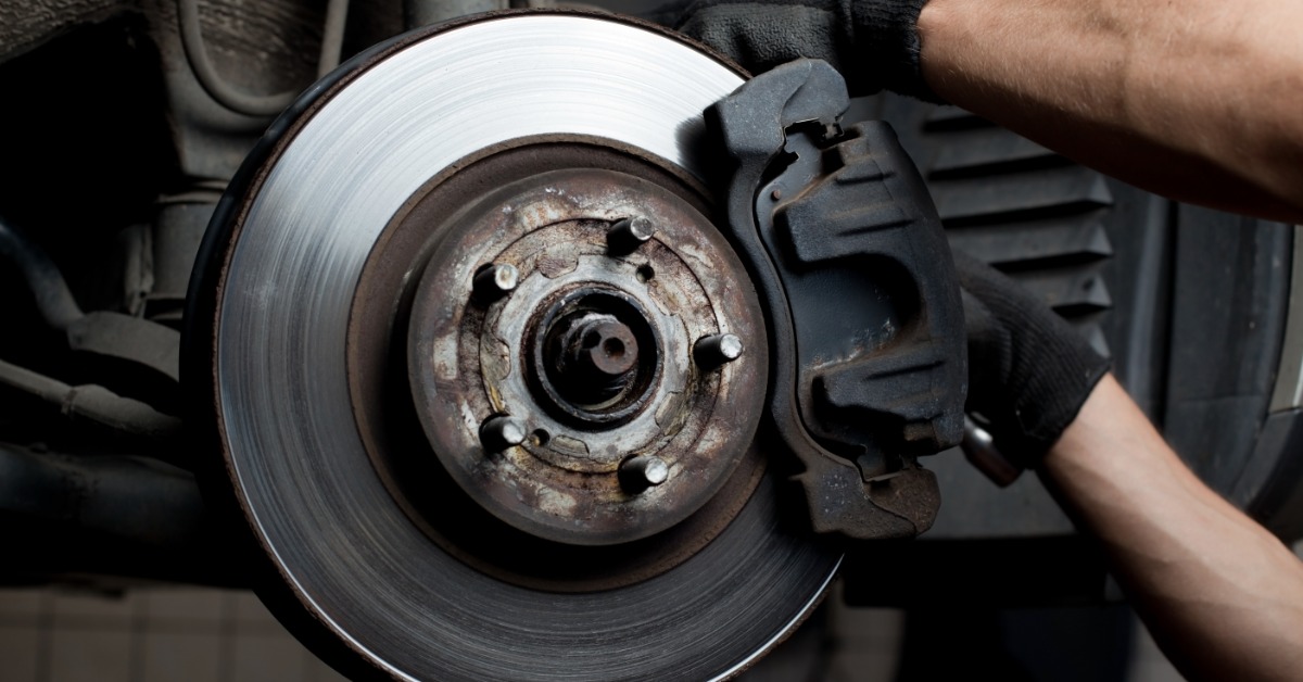 A person wearing blue gloves is installing brake pads on a car wheel assembly inside an automotive repair garage.