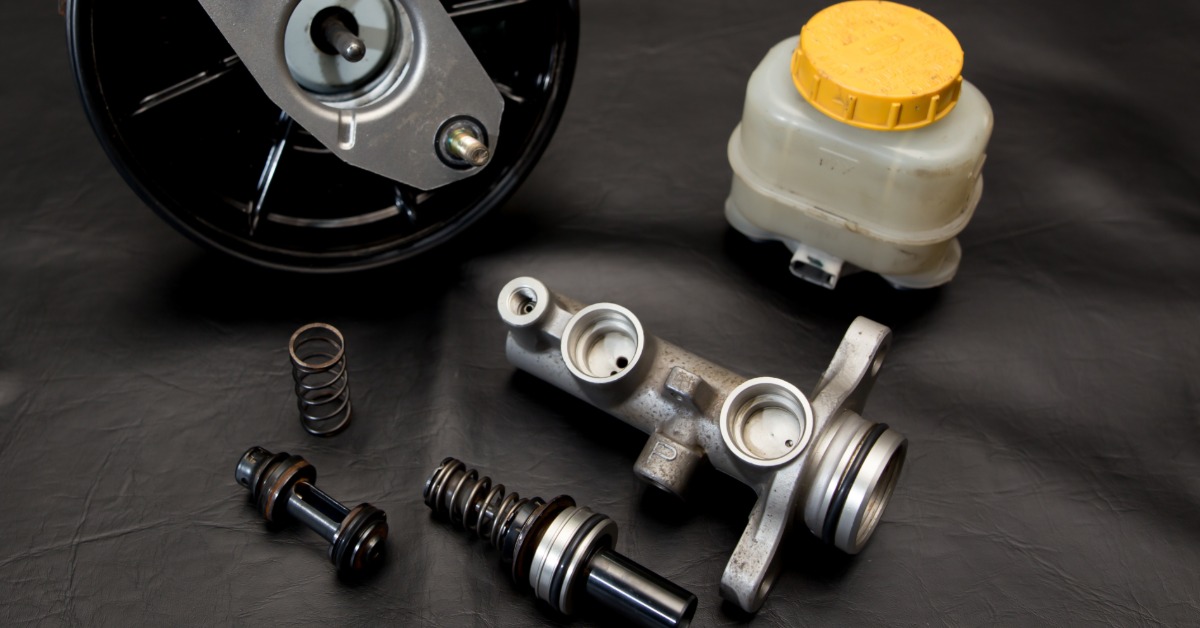 A master cylinder brake set and small metal components are arranged on black leather with soft visible shadows.